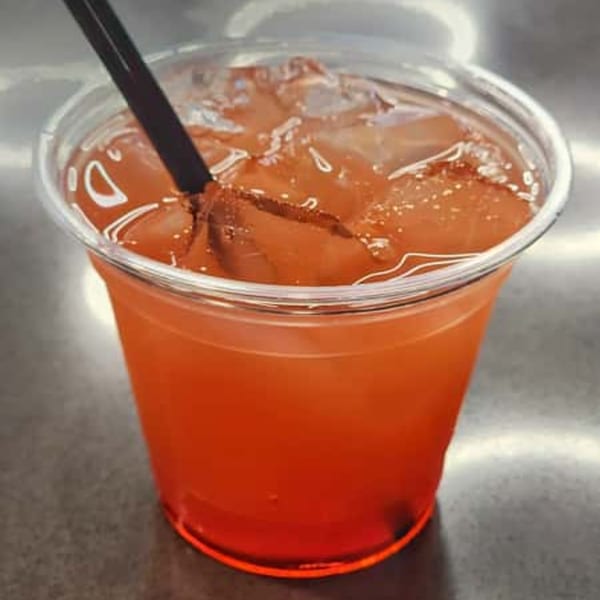 A clear plastic cup filled with a reddish-orange drink, ice, and a black straw.
